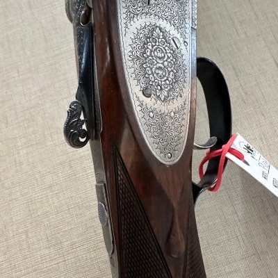 Rifle ou espingarda com metal gravado e cabo em madeira escura com etiqueta branca e cordão vermelho