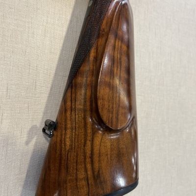 Coronha de arma de fogo em madeira polida com detalhes escuros e padrão quadriculado.