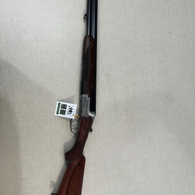 Espingarda de cano duplo com coronha em madeira escura e detalhes metálicos prateados com etiqueta LEGACY 2022.