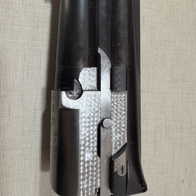 Parte daço de arma de fogo em metal preto e prateado sobre tecido bege.
