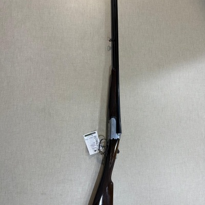 Espingarda de canos duplos com madeira escura e metal preto pendurada numa parede clara