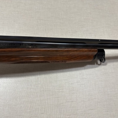 Espingarda com cano preto e coronha de madeira castanha com gravação Benelli