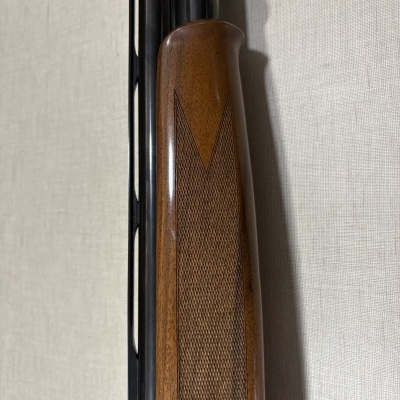 Coronha de madeira castanha e cano metálico escuro de arma apoiada em parede clara