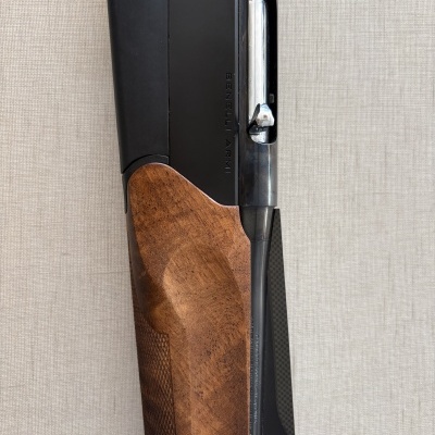 Parte de espingarda com coronha em madeira castanha e aço preto com inscrição BENELLI ARMI.