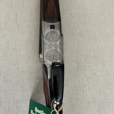 Espingarda com cabo de madeira castanho e corpo metálico gravado, etiqueta verde de identificação