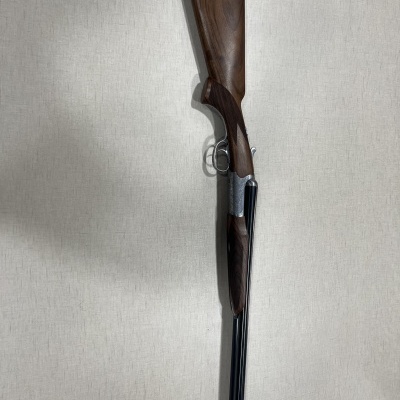 Espingarda com coronha de madeira e canos pretos pendurada na parede