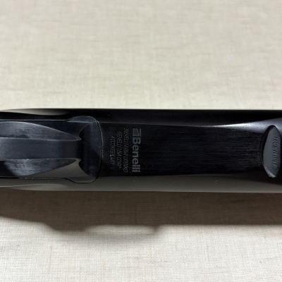 Espingarda Benelli com madeira e metal preto com texto gravado e etiqueta MADE IN ITALY.