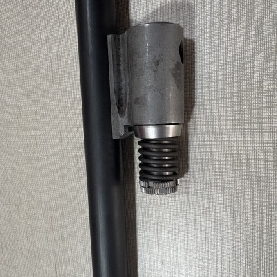 Fixador metálico cinzento com mola ao lado de tubo preto