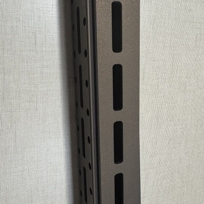 Estrutura metálica preta com orifícios contra parede cinza texturizada