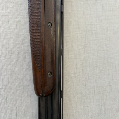 Parte dianteira de uma espingarda com coronha em madeira escura e cano metálico preto