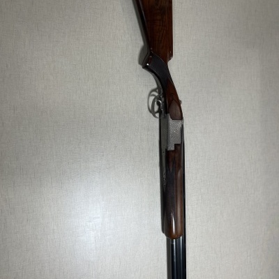 Espingarda de cano duplo com madeira escura e metálica encostada numa parede