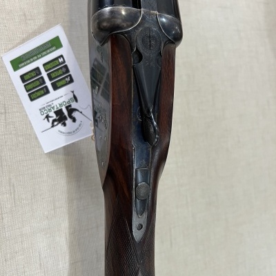 Espingarda de canos duplos em metal escuro com coronha em madeira e etiqueta ao lado