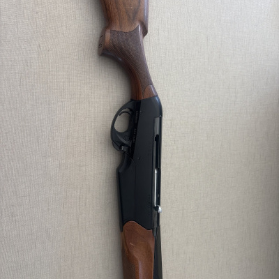 Rifle com coronha em madeira castanha e guarda-mato em metal preto sobre fundo cinza claro