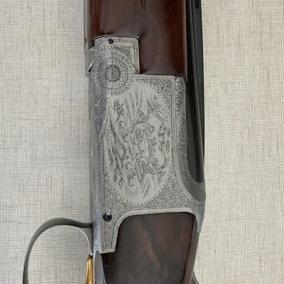 Arma de caça com punho em madeira castanha, corpo metálico gravado e gatilho dourado