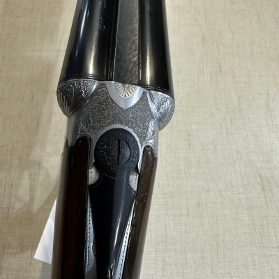 Espingarda de canos duplos com detalhes gravados em metal prateado e coronha em madeira escura