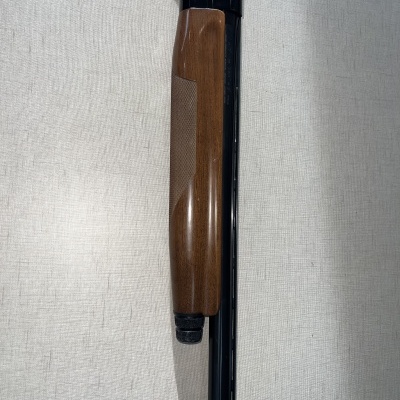 Espingarda com cabo em madeira castanha e corpo preto sobre fundo cinza claro