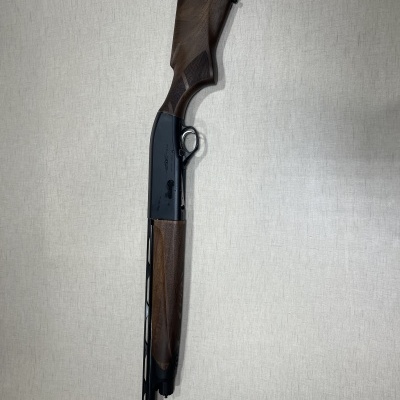 Espingarda com madeira castanha e metal preto contra parede clara