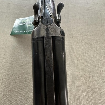 Espingarda dupla de canos paralelos em metal preto e prateado com etiqueta verde