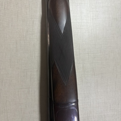 Parte frontal de espingarda com cabo em madeira escura e detalhes metálicos