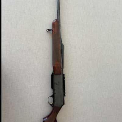 Espingarda de caça com madeira castanha e armação preta contra parede cinza