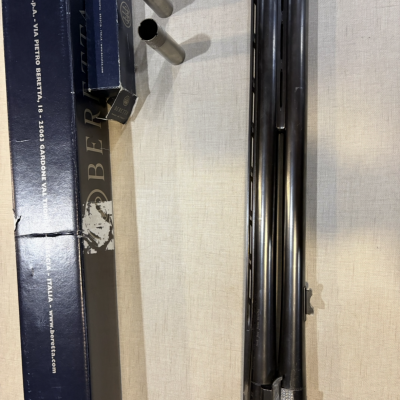 Peças metálicas e caixa azul com texto branco da marca Pietro Beretta junto a arma de canos duplos