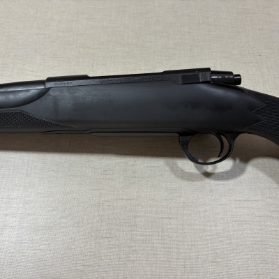 Arma de fogo preta com punho texturizado e gravações em superfície clara.