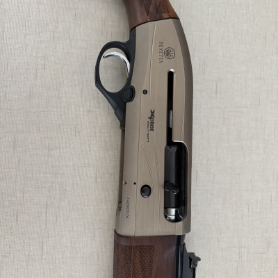 Espingarda Beretta em metal cinzento e madeira castanha com gatilho prateado sobre fundo bege
