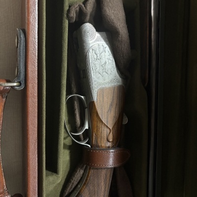 Espingarda com ação gravada em metal e coronha de madeira dentro de estojo verde