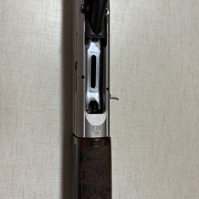 Imagem de uma arma com empunhadura de madeira escura e parte metálica prateada contra fundo cinza