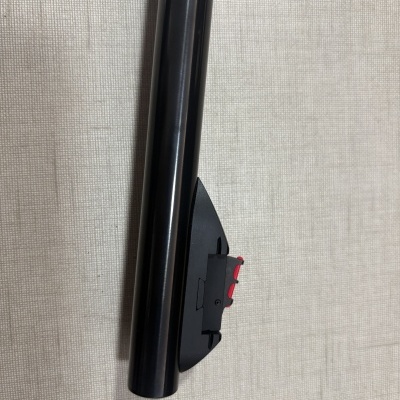 Tubo preto com suporte preto e detalhe vermelho numa superfície clara texturada.