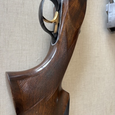 Empunhadura de arma de fogo de madeira castanha com gatilho dourado e detalhes metálicos