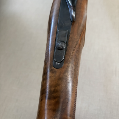 Espingarda com coronha em madeira castanha e centro metálico preto.
