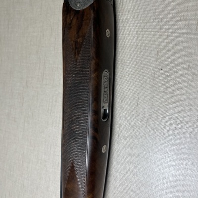 Parte da coronha de uma espingarda em madeira castanho escuro e metal cinzento