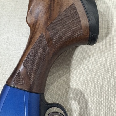 Coronha de madeira castanha com textura, guarda-mato preto e parte azul de rifle com disparador metálico