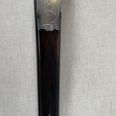 Parte superior de espingarda dupla com metal gravado e coronha em madeira escura trabalhada