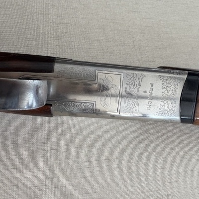 Espingarda com metal gravado e punho em madeira castanha sobre tecido cinza