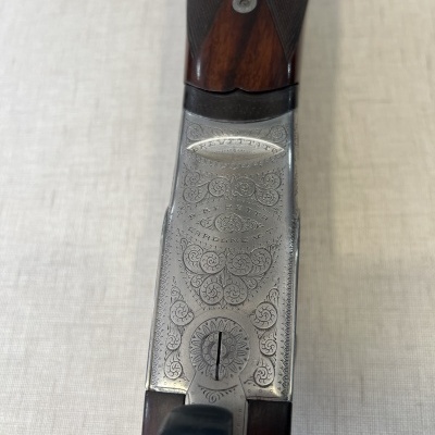 Parte superior de arma de caça com cabo de madeira escura e gravação metálica