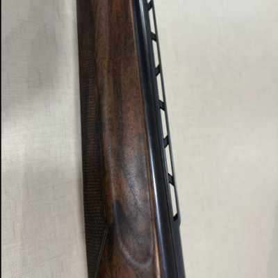 Coronha em madeira escura e cano metálico preto de arma de fogo sobre fundo claro.