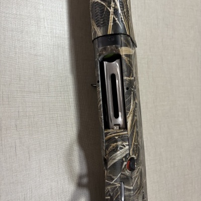 Espingarda camuflada com mecanismo metálico exposto encostada a uma parede cinzenta texturada