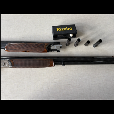 Canhão de arma de fogo desmontado com madeira e metal, caixa Rizzini e acessórios cilíndricos sobre superfície clara.