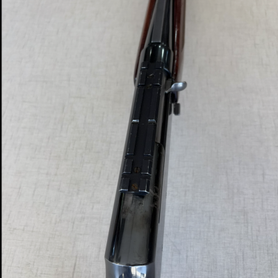 Espingarda de cano preto e madeira castanha sobre superfície clara