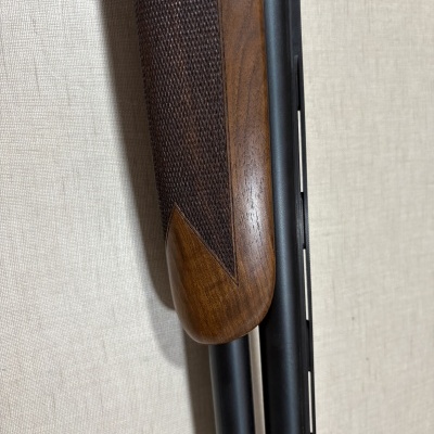 Cabo de arma em madeira castanha com cano duplo em metal preto numa parede bege