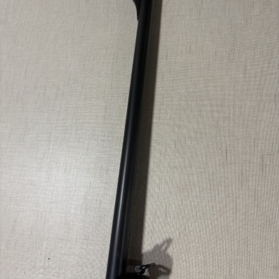 Arma de fogo com cano longo preto e cabo de madeira castanha sobre superfície branca.