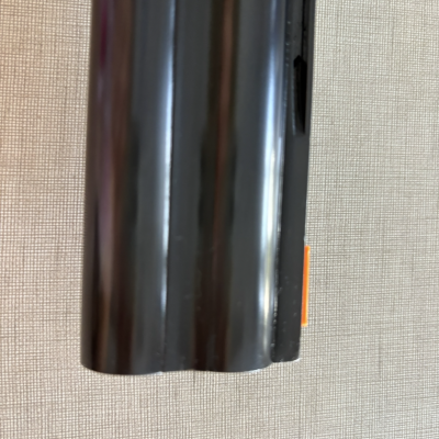 Objeto cilíndrico metálico preto com etiqueta laranja sobre superfície bege texturizada