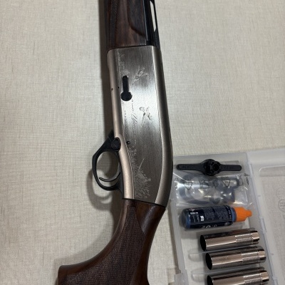 Espingarda com coronha de madeira e metal prateado com gravações, e acessórios num estojo plástico