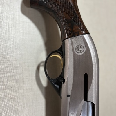 Detalhe de arma de fogo Beretta com coronha em madeira escura e corpo metálico prateado