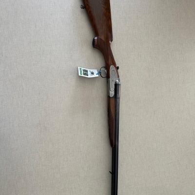 Espingarda de canos duplos com coronha de madeira castanha e canos negros pendurada numa parede clara