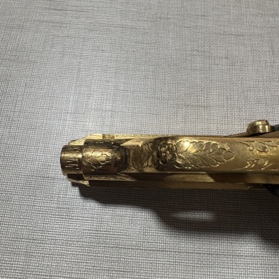 Detalhe da parte frontal de arma dourada decorativa com gravuras florais sobre superfície cinza