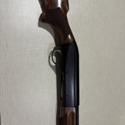 Espingarda com coronha de madeira castanha e metal preto, texto BENELLI ARMI URBINO - MADE IN ITALY