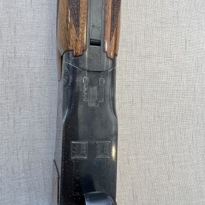 Espingarda com madeira castanha e armação metálica preta com gravações sobre fundo cinza.